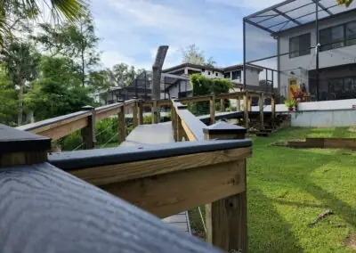 Wooden ramp walkway with railing across a sloped lawn behind a modern home