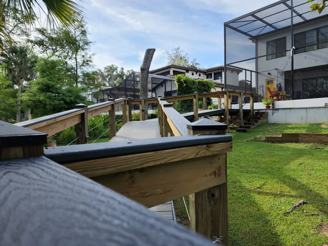 Wooden ramp walkway with railing across a sloped lawn behind a modern home