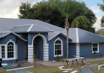 Blue stucco home with a new standing-seam metal roof, roofing panels on the lawn
