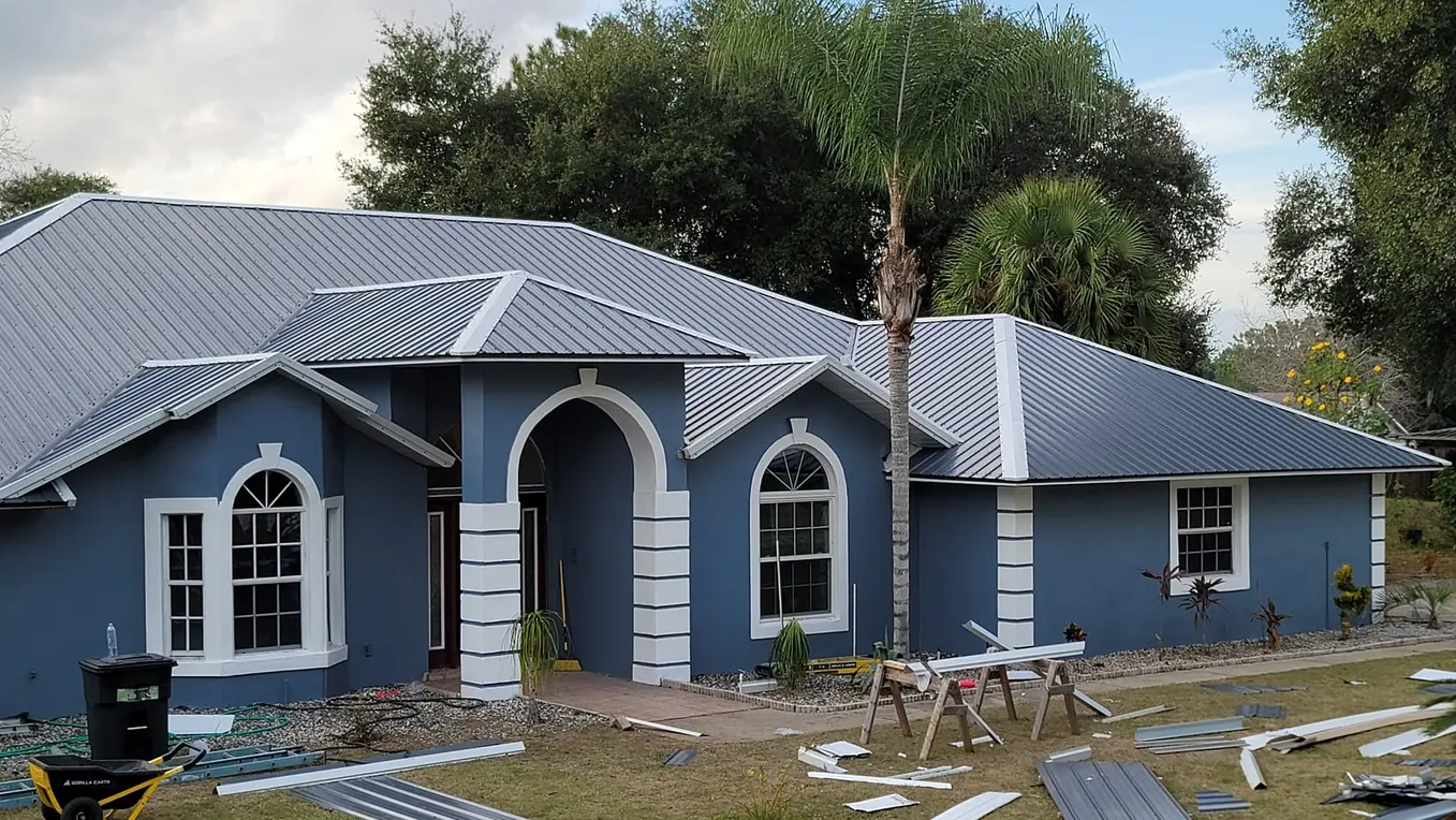 Blue stucco home with a new standing-seam metal roof, roofing panels on the lawn