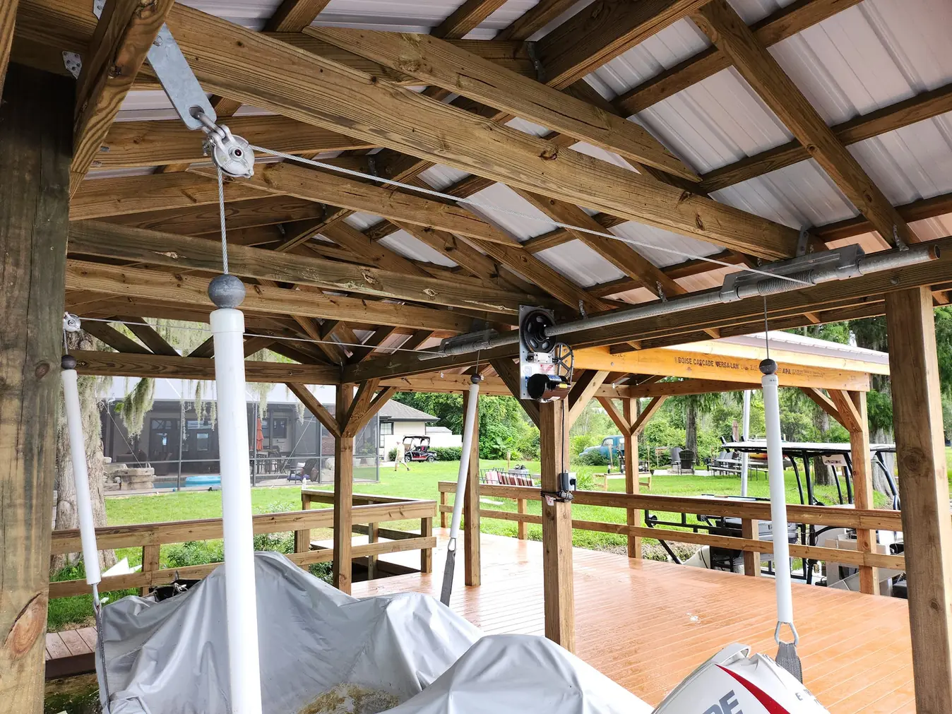 Boathouse ceiling with lift motor, cables and pulleys above a covered boat