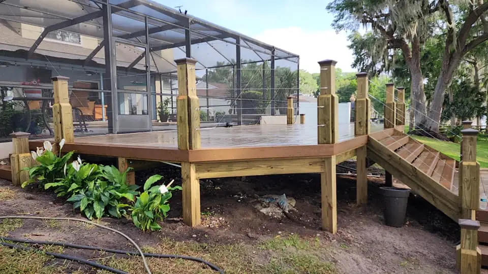 New composite deck with wooden posts, cable railing and stairs beside a pool enclosure