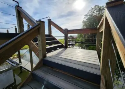 View down composite dock stairs with wood and cable railing toward a lake