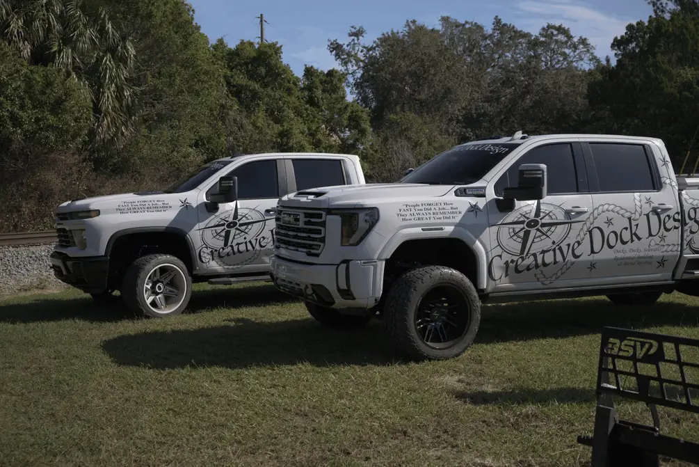 Two white Creative Dock Design pickup trucks with company graphics parked on grass
