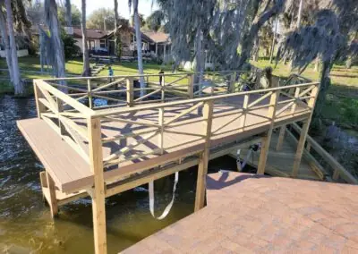 New wooden dock platform with X-pattern railing over a lake beside a paver patio