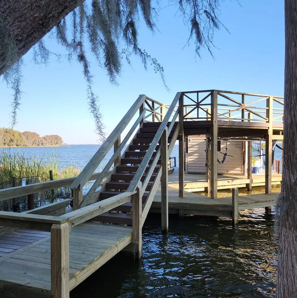 Wooden dock with stairs to a two-story boathouse sundeck on a lake
