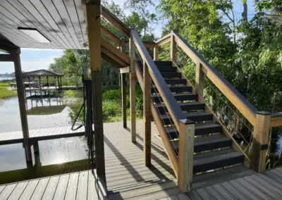 Wooden stairs with cable railing rising from a dock to a boathouse upper deck