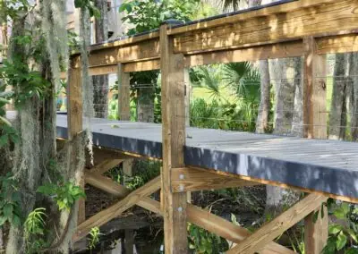 Elevated wooden boardwalk with gray decking and railing through wooded wetland