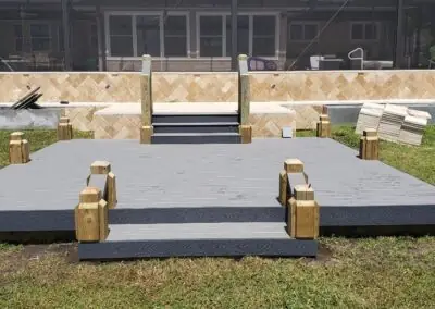 Gray composite deck with wooden post caps and steps up to a stone-faced patio