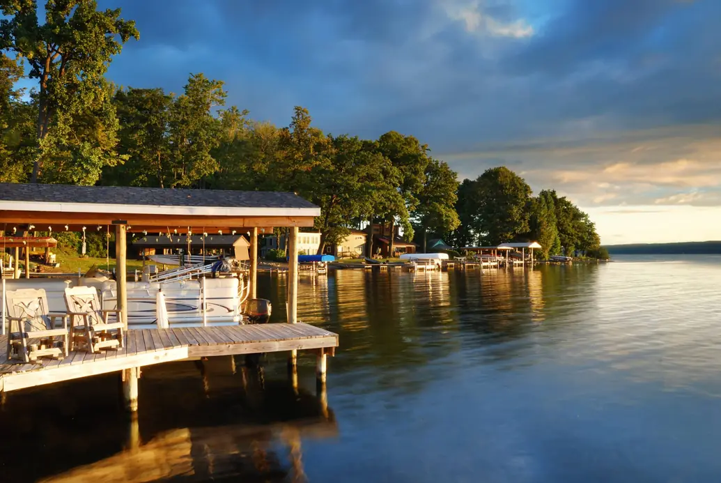 Covered boat lift with a pontoon boat and Adirondack chairs on a lake dock at sunset