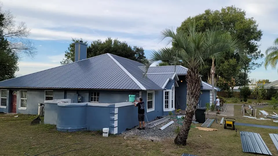 Crew working on a blue home during a metal roof installation