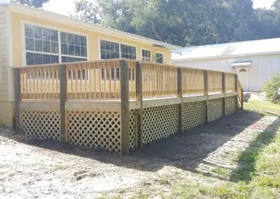 Wooden deck with spindle railing and lattice skirting along a yellow house