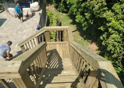 New wooden stairs with railings leading down from a paver pool deck